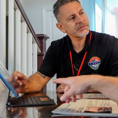 Man in black shirt discussing a brochure at a table with a tablet, indoors.